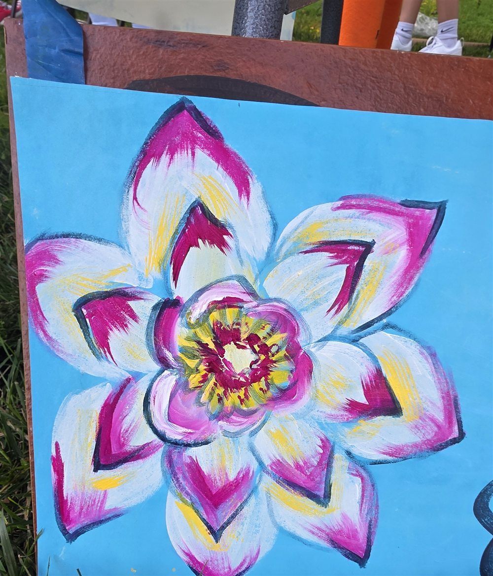 A finished panel propped on a wooden frame: a lotus flower in white, magenta and yellow on a bright blue ground.