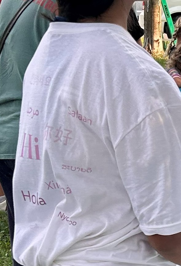 The back of a white project t-shirt printed with greetings in many languages, worn at the paint day.